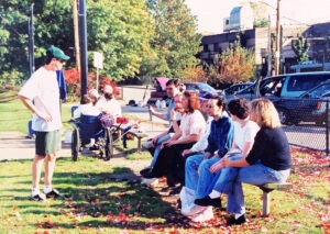 in 2000, Rob Weissman stands in front of a bench in Brookline talking to John Oliveira and some friends watching the Renegades take on the Lowell LAB Retrievers
